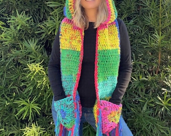 May include: A colorful crocheted hooded scarf with pockets and fringe. The scarf is made in shades of green, yellow, pink, and blue.