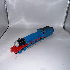 May include: A blue toy train with a black roof and red detailing. The train features a smiling face and the number 4. A classic children's toy, the train is a popular item.
