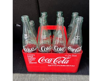 Paquete de 8 botellas de vidrio vintage de Coca-Cola de 16 oz con caja de transporte de plástico rojo.