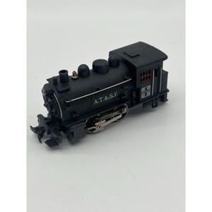 Op de afbeelding: Een zwarte modeltreinlocomotief met de tekst "A.T.&S.F." aan de zijkant. Het model heeft gedetailleerde kenmerken, waaronder een cabine, schoorsteen en wielen. De trein staat tegen een witte achtergrond.