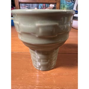 May include: A sage green ceramic planter with a basket weave design on the lower portion and a ridged texture on the upper portion. The planter has a wide top and a narrower base, suitable for indoor or outdoor use.