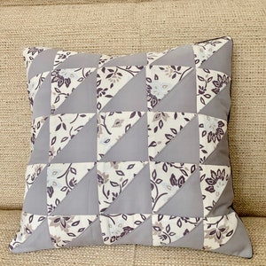 May include: A grey and white patterned cushion with a geometric design. The cushion is made of fabric and has a square shape.