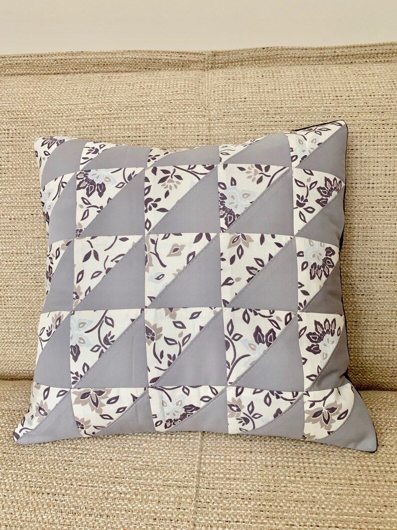 May include: A grey and white patterned cushion with a geometric design. The cushion is made of fabric and has a square shape.
