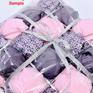 Op de afbeelding: Een doorzichtige plastic zak gevuld met roze en paarse vierkante stoffen, vastgebonden met een zilveren lint. De zak is gelabeld met "Packing Sample".