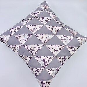 May include: A grey and white patterned cushion with a geometric design. The cushion is made of fabric and has a square shape.