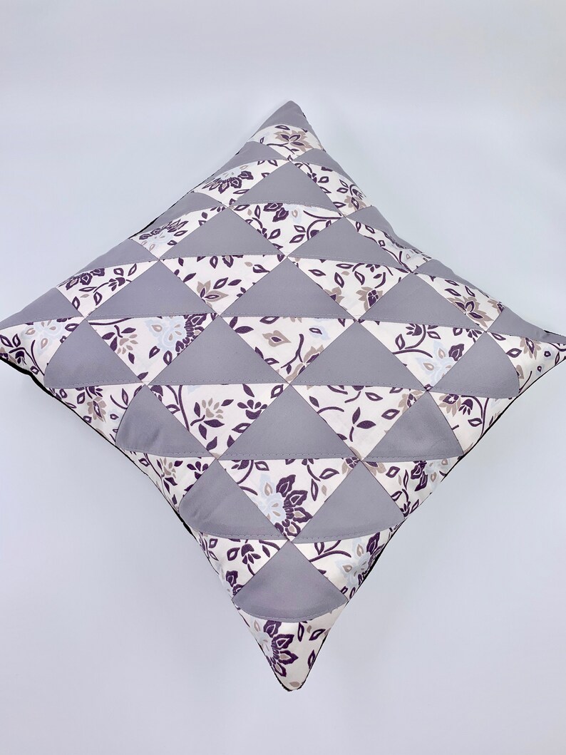 May include: A grey and white patterned cushion with a geometric design. The cushion is made of fabric and has a square shape.