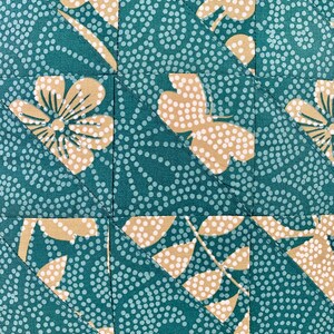 以下が含まれることがあります： 白のドット柄とベージュの花柄が施されたターコイズブルーの生地。生地は三角形にカットされ、パッチワークパターンになるように縫い合わされています。