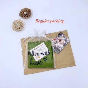 May include: An overhead shot shows a package with a green insert in a sheer white bag, a floral card, and two decorative flower pins. The bag reads "Filled with Love" in black script. The words "Regular packing" are in red.