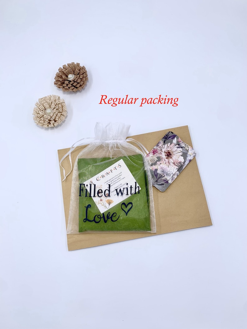 May include: An overhead shot shows a package with a green insert in a sheer white bag, a floral card, and two decorative flower pins. The bag reads "Filled with Love" in black script. The words "Regular packing" are in red.