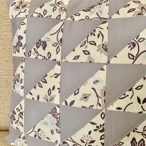May include: A grey and white patterned cushion with a geometric design. The cushion is made of fabric and has a square shape.