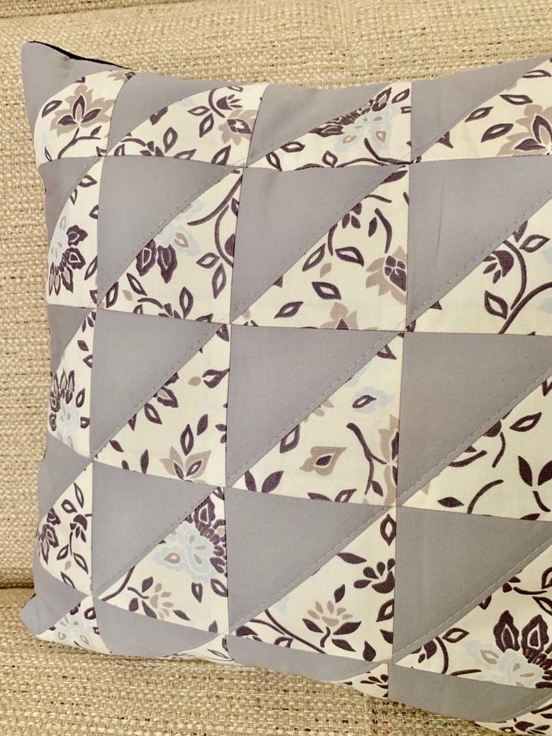 May include: A grey and white patterned cushion with a geometric design. The cushion is made of fabric and has a square shape.