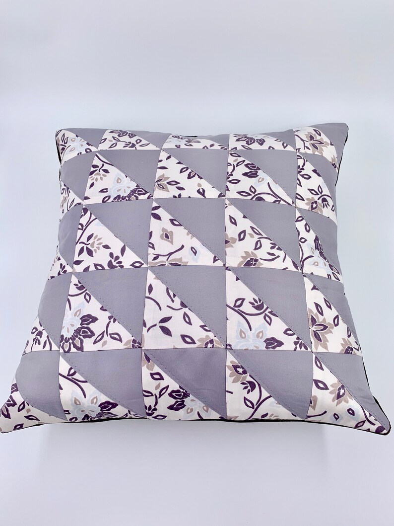 May include: A grey and white patterned pillow with a geometric design. The pillow is made of fabric and has a black trim.