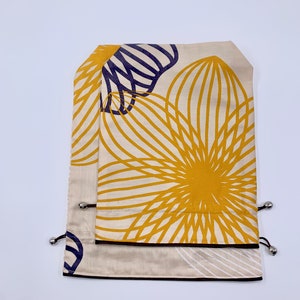 May include: Two beige fabric drawstring bags with a floral design in yellow and navy blue. The bags have a black border and silver metal accents.