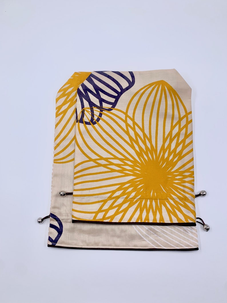 May include: Two beige fabric drawstring bags with a floral design in yellow and navy blue. The bags have a black border and silver metal accents.