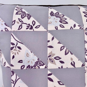 May include: A grey and white patterned cushion with a geometric design. The cushion is made of fabric with a floral pattern and is sewn together in a patchwork style.