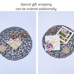 May include: Two gift boxes, one gold and one white, are presented on a dark gray woven placemat. The gold box is tied with a cream ribbon, and the white box has a floral design and a cream ribbon. The text "Special gift wrapping can be ordered additionally" is at the top.