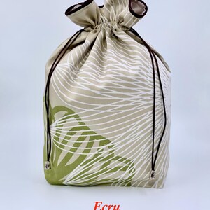 May include: An ecru-colored drawstring bag with a botanical pattern in white and green. The bag has a brown drawstring and trim. The word "Ecru" is printed at the bottom of the bag.