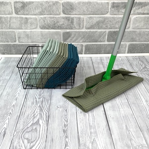 Può includere: Un cesto di filo nero contenente una pila di panni per la pulizia verdi, blu e grigi, accanto a uno straccio verde e argento con una testa in microfibra grigia.