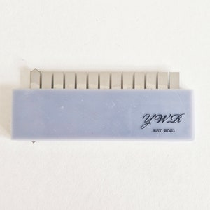 May include: A close-up of a silver metal comb with 15 teeth. The comb is attached to a light purple plastic base with the text "YWR EST 2021" printed on it.