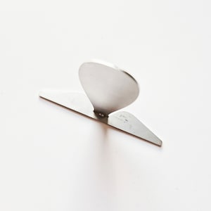 May include: A silver metal bottle opener with a teardrop-shaped handle and a flat, triangular base.