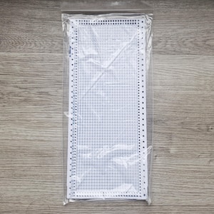 May include: A white plastic knitting pattern chart with a grid design and numbered rows and columns, packaged in a clear plastic sleeve. The chart is designed for use in knitting projects.
