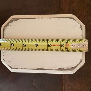 May include: A rectangular, off-white wooden sign with a distressed, grey-edged border. A yellow tape measure shows the sign is approximately 18 cm long. The sign has a blank surface, ready for customization.