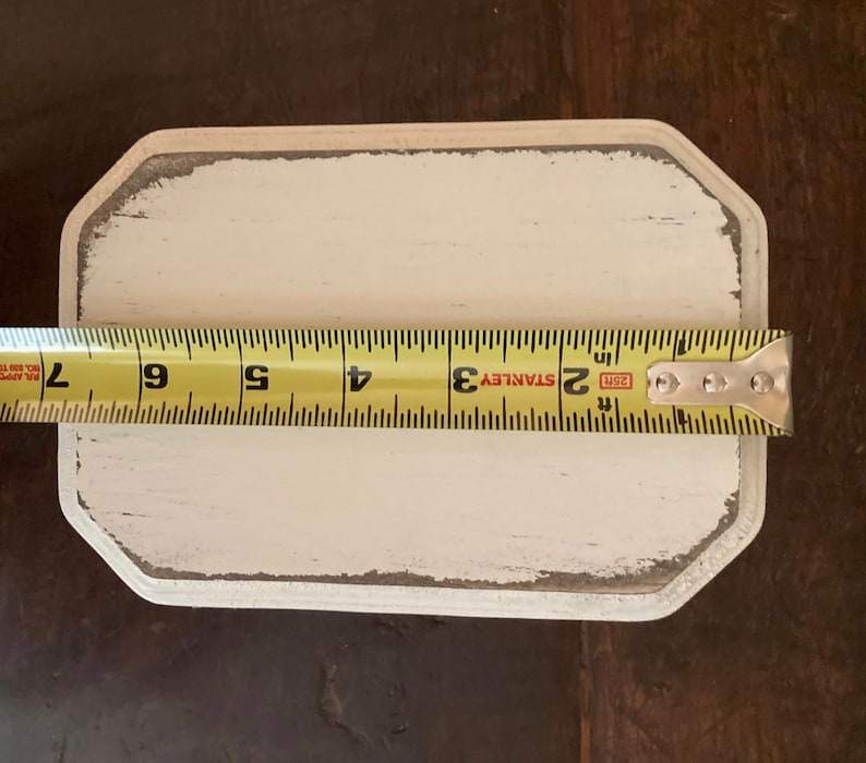 May include: A rectangular, off-white wooden sign with a distressed, grey-edged border. A yellow tape measure shows the sign is approximately 18 cm long. The sign has a blank surface, ready for customization.