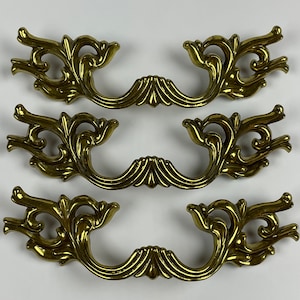 May include: Three ornate gold-toned cabinet pulls with a decorative floral design.