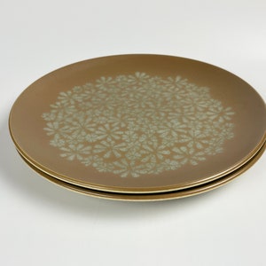 May include: Two brown ceramic plates with a white floral pattern. The plates are stacked on top of each other.