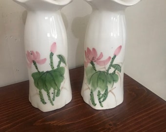 Puede incluir: Un par de jarrones de cerámica blanca con un borde superior rizado y un diseño floral. Los jarrones están decorados con flores de loto rosas y verdes.