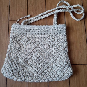 May include: A white crocheted bag with a diamond pattern and a long strap.