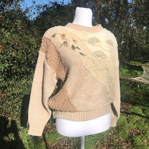 May include: A beige, cream, and brown knitted sweater with a floral design and beaded embellishments.