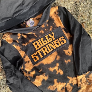 May include: Black and orange tie-dye hoodie with a black patch that says "BILLY STRINGS" on the front.
