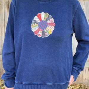 May include: A dark blue denim sweatshirt with a colorful patchwork flower design on the front.