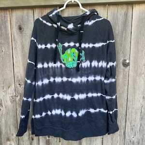 May include: Black and white tie-dye hoodie with a green and white graphic of a fish on the front. The hoodie has a drawstring hood and a kangaroo pocket.