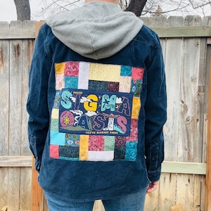 May include: A navy blue corduroy shirt with a gray hooded sweatshirt attached. The back of the shirt features a colorful patchwork design with the text "Sigma Oasis" and "You're Already There".