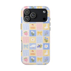 May include: A pastel-colored phone case with a patchwork design. The case features squares with illustrations of strawberries, flowers, bows, cakes, and ducks. The case has a camera cutout for a triple-lens camera.