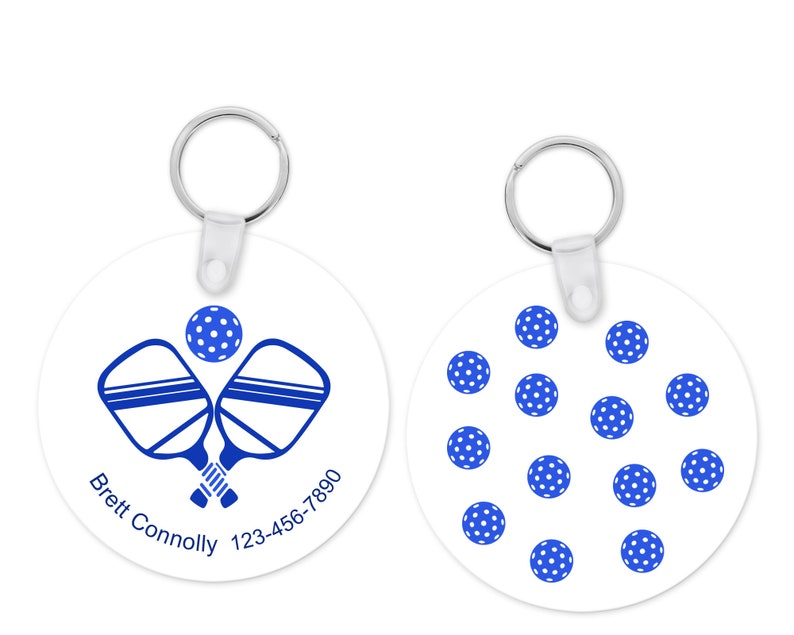 Pu&ograve; includere: Portachiavi rotondo bianco con un design pickleball blu. Un lato presenta racchette incrociate e una palla, con testo. L'altro lato ha un motivo di palline da pickleball blu e bianche. Include un portachiavi in metallo.