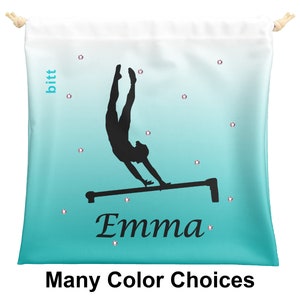Puede incluir: Una bolsa de cordón de color turquesa y blanco con una silueta de una gimnasta en las barras asimétricas. La bolsa tiene el nombre "Emma" impreso en ella.