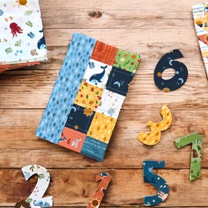 Könnte beinhalten: Eine gesteppte Bibel-Hülle mit Patchwork-Design mit Walen, Blumen und anderen Mustern. Die Hülle ist geöffnet und zeigt das Innere. Dekorative Zahlen-Ausschnitte und der Text "Sew a Story" sind ebenfalls sichtbar.