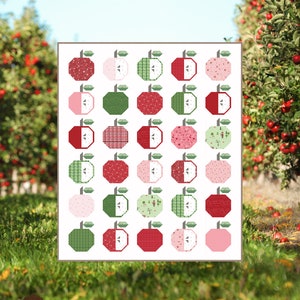 May include: A quilt pattern titled "Apple Season" featuring a grid of stylized apple designs in various colors and patterns. The quilt pattern includes a table runner, crib, and lap size. The image also includes the text "Sew a Story".