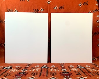 May include: Two blank white canvases, each measuring approximately 12 inches by 16 inches, are displayed on a patterned orange fabric.