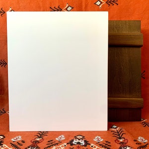 May include: A white canvas board with a brown wooden frame. The board is sitting on a red and white patterned fabric.