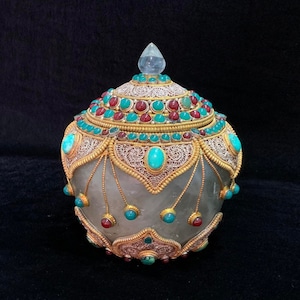 May include: An ornately decorated, white, jeweled box with a lid. The box is decorated with gold and silver filigree and turquoise and red gemstones.