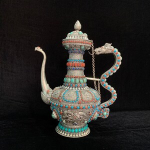 Könnte beinhalten: Eine silberne Teekanne mit einem drachenförmigen Griff, verziert mit Türkis- und Korallensteinen. Die Teekanne hat einen Ausguss und einen Deckel mit einem Knauf.