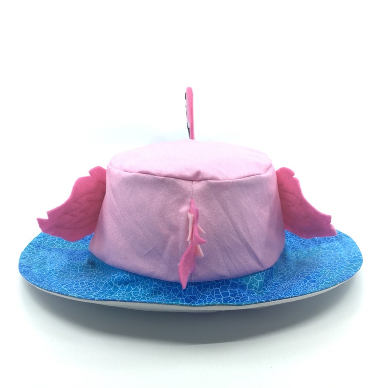 Puede incluir: Un sombrero de flamenco rosa con un ala azul estampada. El sombrero presenta alas y cola rosas, y una peque&ntilde;a cabeza de flamenco. El sombrero est&aacute; dise&ntilde;ado para ser usado en la cabeza.