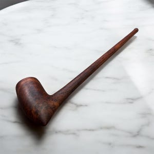 Puede incluir: Una pipa de madera marrón oscuro con un cuenco curvado y un tallo largo y delgado. La pipa está hecha de una madera rica y oscura con patrones de vetas visibles. La pipa descansa sobre una superficie de mármol blanco.
