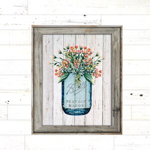 Op de afbeelding: Een blauwe mason jar met witte letters die "Ball Perfect Mason" lezen, gevuld met roze en witte bloemen tegen een witte houten achtergrond.