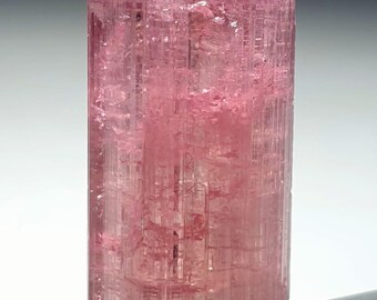 May include: A pink tourmaline crystal with a clear, faceted, and elongated shape. The crystal has a smooth, polished surface and a translucent appearance.