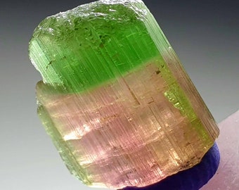 May include: A green, pink, and brown tourmaline crystal with striations. The crystal is translucent and has a pointed end.